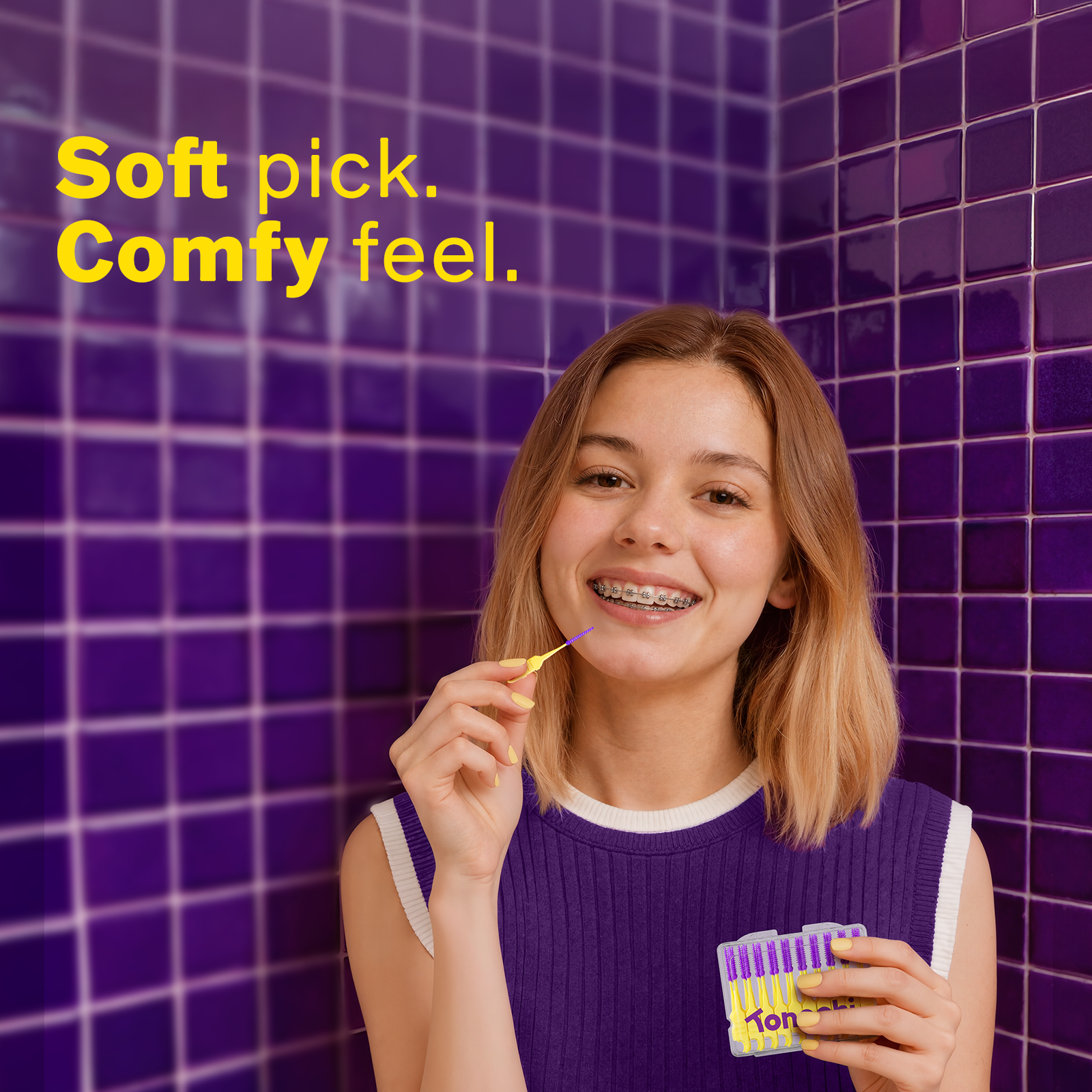Woman with braces holding a dental pick against a purple tiled wall.