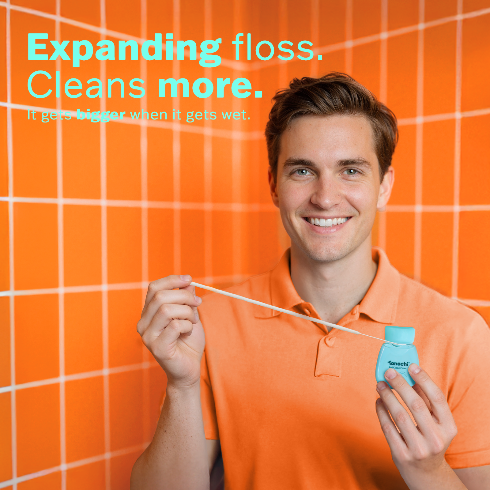 Smiling man in orange shirt holding Tonochi expanding dental floss against orange tiled wall with text "Expanding floss. Deep clean."