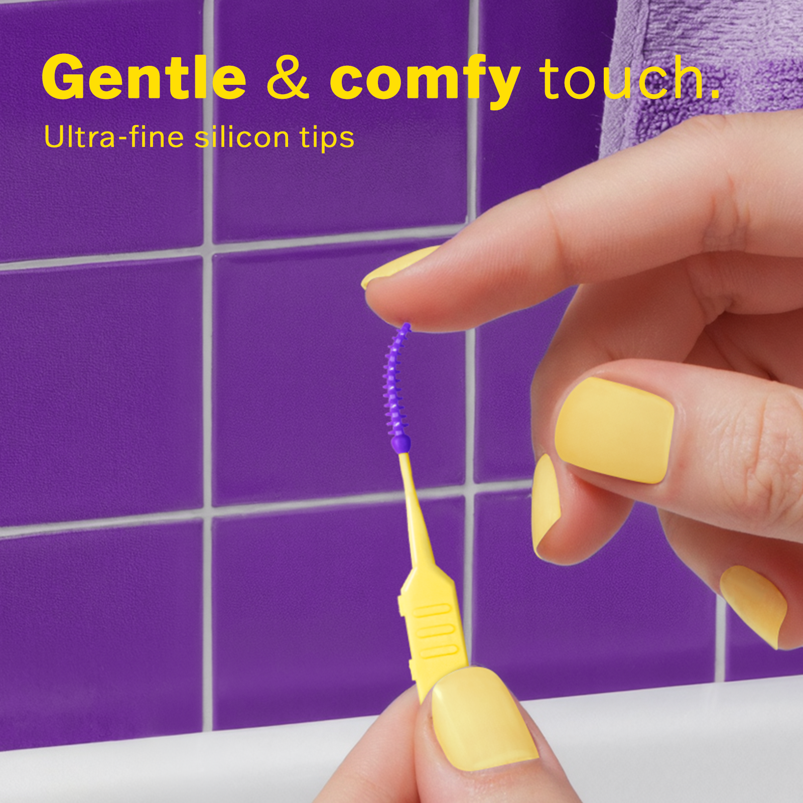 Close-up of hands with yellow nail polish holding a purple ultra-fine silicon tip interdental brush against purple tile background