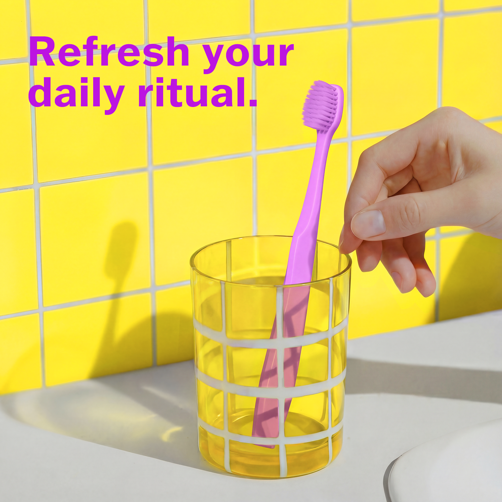 Hand placing a lavender toothbrush into a yellow glass with a yellow tiled wall background.