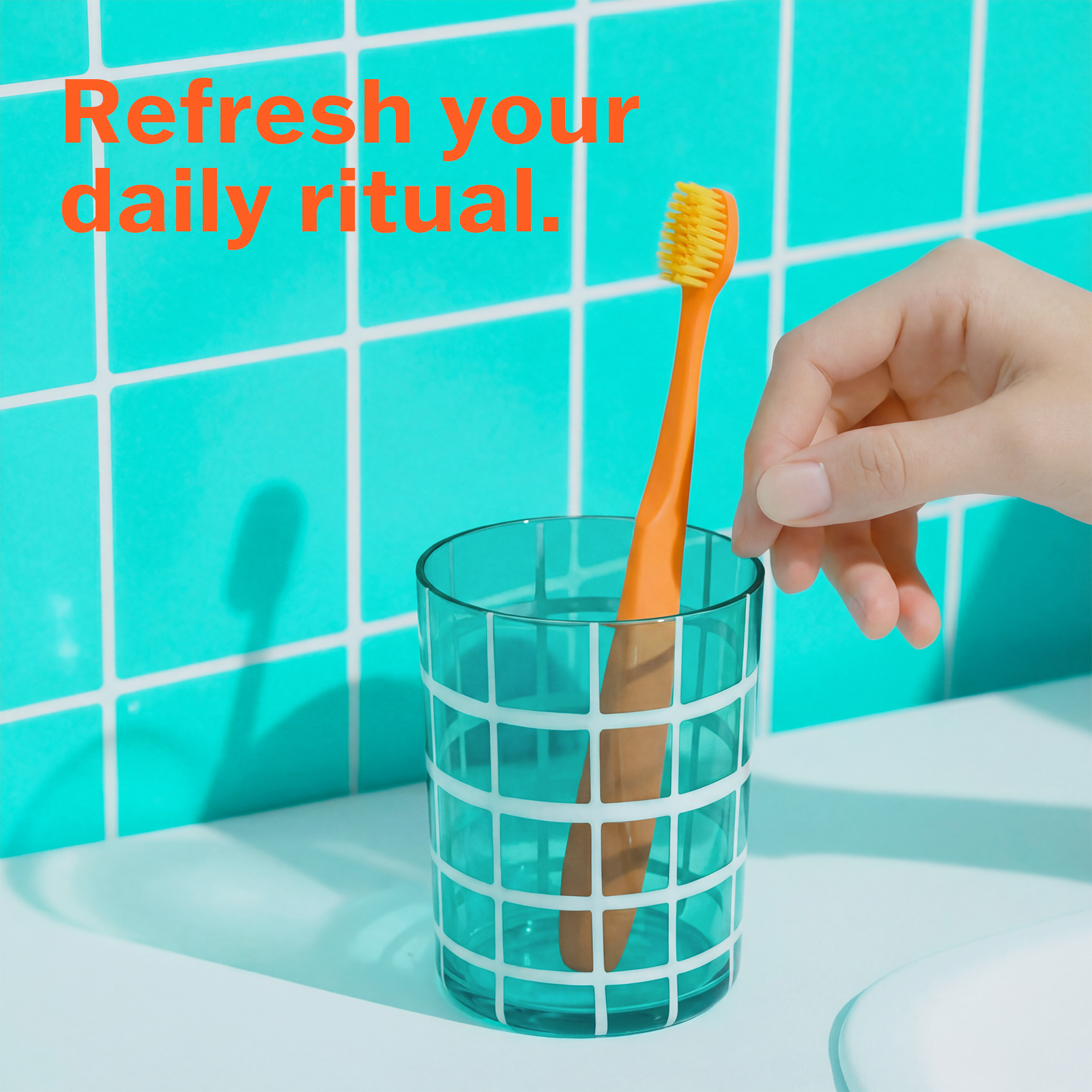 Hand placing an orange toothbrush into a green glass with a green tiled wall background.